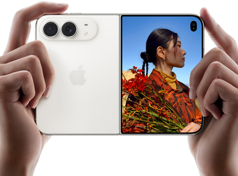 Due mani tengono un iPhone Duo bianco stellare in orizzontale, aperto; sul pannello sinistro si nota la doppia fotocamera posteriore Fusion da 48MP, mentre sul pannello destro si vede una persona che si fa fotografare sullo schermo esterno; il soggetto può vedere il proprio volto mentre viene scattata la foto grazie alla funzione Duo Preview