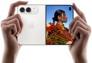 Due mani tengono un iPhone Duo bianco stellare in orizzontale, aperto; sul pannello sinistro si nota la doppia fotocamera posteriore Fusion da 48MP, mentre sul pannello destro si vede una persona che si fa fotografare sullo schermo esterno; il soggetto può vedere il proprio volto mentre viene scattata la foto grazie alla funzione Duo Preview