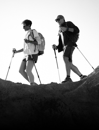 Due persone con Apple Watch al polso che fanno trekking su un sentiero roccioso con racchette e attrezzatura